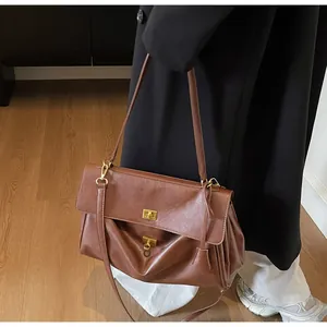 Detailed side view of dark brown leather tote featuring gold lock and accordion folds