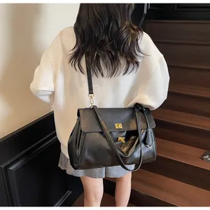 Rear view of a large black tote bag with gold metal hardware worn on a wood staircase