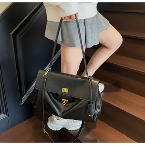 Close-up of a large black leather tote bag with gold metal clasp on a model in lifestyle setting