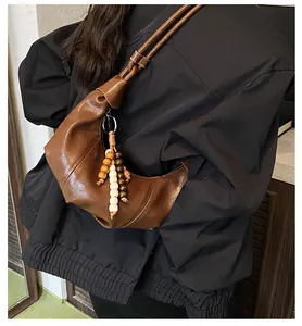 Close-up of a dark brown crescent bag with unique wooden bead charm and soft PU texture