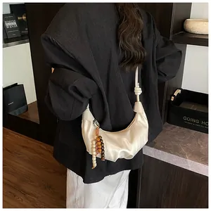 Detail of off-white pleated hobo bag with wood bead charm and knotted shoulder strap