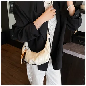 Detail of a creamy white dumpling bag with leather strap and decorative wood beads