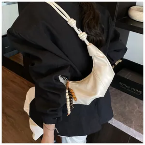 Detail of cream crescent bag with wood bead tassel and knot strap on black blazer