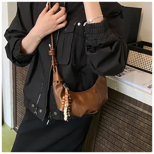 Detail of a dark brown crescent bag featuring matte leather texture and a beaded tassel charm