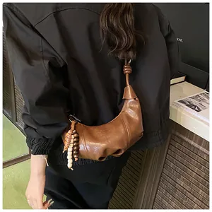 Detail of brown croissant bag with pleated texture and bohemian beaded tassel accessory