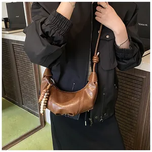 Detail of a brown leather dumpling bag with side beads and knotted shoulder strap