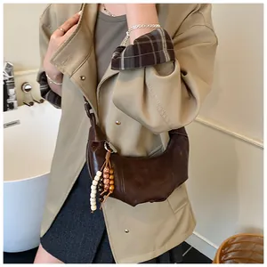 Close-up of brown crescent crossbody bag with pleated leather and beaded tassel detail