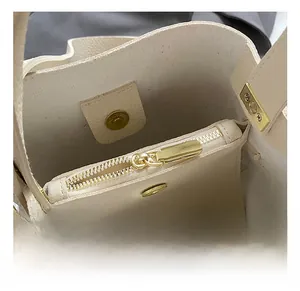 Detail view of beige bucket bag showing gold magnetic buckle and lychee leather texture