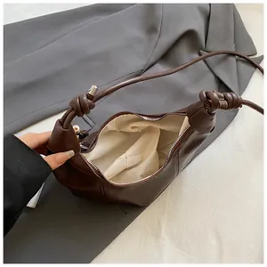 Detail of dark brown dumpling bag featuring knotted shoulder straps and silver zipper