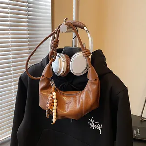 Brown pleated half-moon bag with knotted strap and wooden beads in casual setting