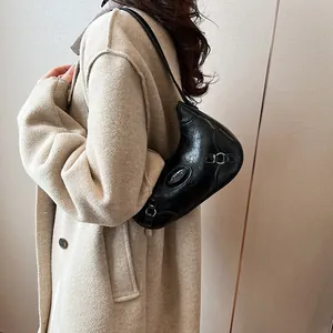 Minimalist black asymmetrical shoulder bag with silver rings on a beige coat model