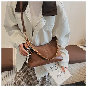 Détail d'un sac seau marron avec chaîne en métal, daim texturé et perles en bois