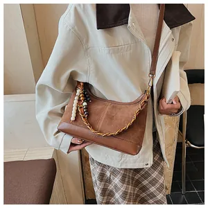 Détail du sac seau en daim avec chaîne dorée et perles décoratives dans un café chic