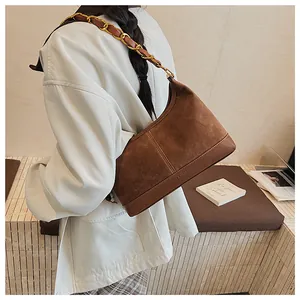 Gros plan du sac seau en daim marron avec chaîne dorée sur l'épaule d'un modèle