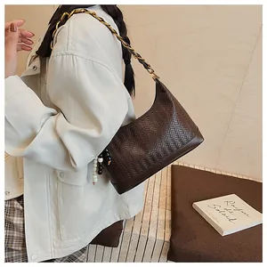 Détail du sac seau marron foncé avec chaîne dorée et breloque à pompon en perles
