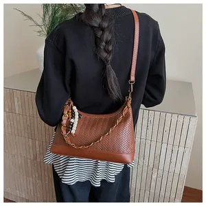 Gros plan du sac seau en cuir tressé marron avec chaîne dorée et breloque en perles colorées