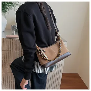 Sac seau en daim marron avec chaîne dorée et breloque en perles porté par le mannequin