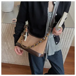 Détail du sac seau en daim et cuir avec chaîne dorée et breloques en perles colorées