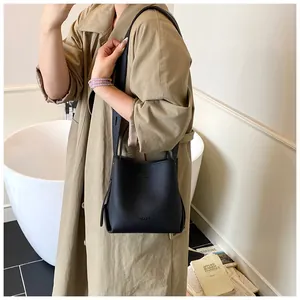 Close-up of black litchi pattern bucket bag with VIVI & BAG lettering on khaki trench coat
