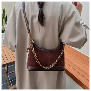 Détail du sac seau marron foncé avec chaîne dorée et pompon perlé sur un mannequin