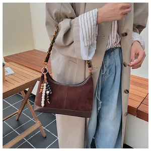 Détail du sac seau en daim marron avec chaîne en métal et pompon perlé multicolore