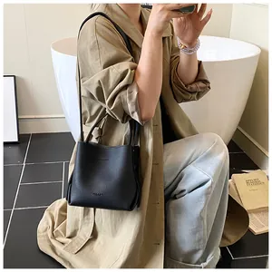 Detail of black lychee grain leather bucket bag featuring top handles and slim shoulder strap