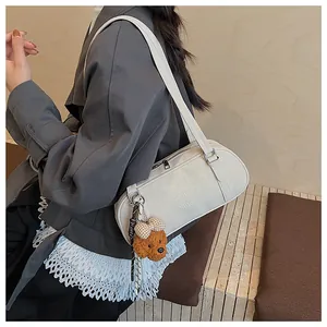 Close-up of cream leather shoulder bag featuring embossed logo and plush bear charm