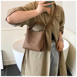 Brown lychee leather bucket bag worn crossbody, showing detachable strap and texture