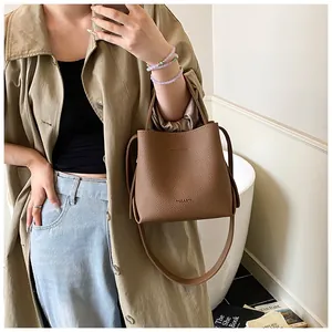 Detail of brown lychee pattern leather bucket bag carried by model in casual trench coat