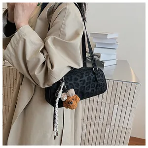 Detail of black leopard print underarm bag with cute plush bear charm on beige trench coat