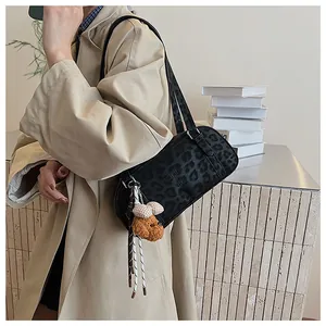 Detail of black leopard print underarm bag with a brown plush puppy charm on beige coat
