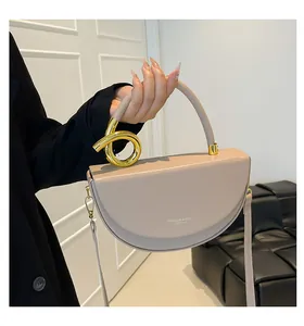 Detail of beige saddle bag featuring gold knot hardware and embossed fashion text