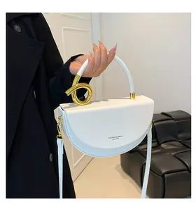 Detail view of white saddle bag showing gold spiral twist hardware and printed logo