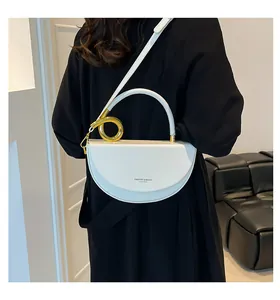 Détail du sac selle blanc avec poignée en anneau doré et logo de mode embossé sur cuir