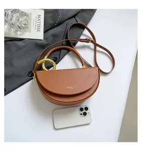 Detailed top view of a brown leather saddle bag with gold rings and fashion accessories