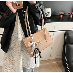 Detail of beige shoulder bag with embossed letters, lace bow and bead chain decoration