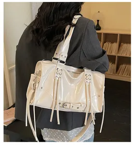 Detail of ivory patent leather shoulder bag with buckle and fringe tassels worn by model