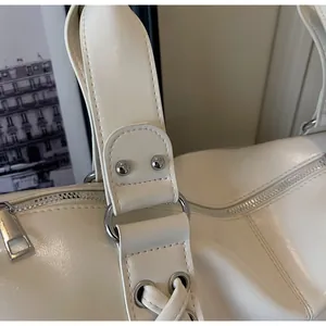 Detail of glossy off-white shoulder bag with silver hardware and lace-up side design