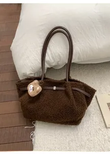 Brown plush tote bag with soft bear charm and long straps in cozy winter setting