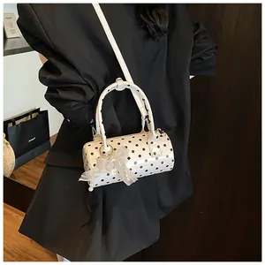 Detalle del bolso cilíndrico blanco con lunares, lazo de encaje y colgante de perla