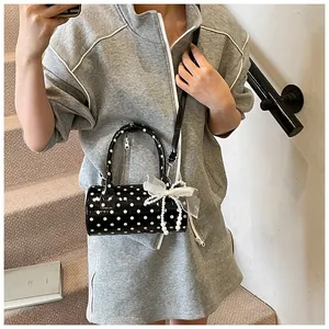 Detalle de bolso cilíndrico de lunares con lazo blanco grande y colgante de perlas