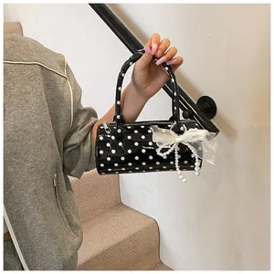 Detalle del bolso cilíndrico negro de lunares con colgante de encaje y perlas