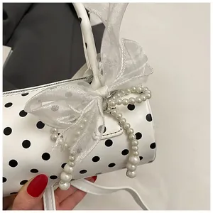 Detalle del bolso cilíndrico de lunares con lazo de organza y borlas de perlas