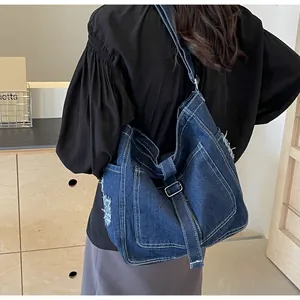 Detail of large denim tote bag featuring distressed edges and front pocket on a model