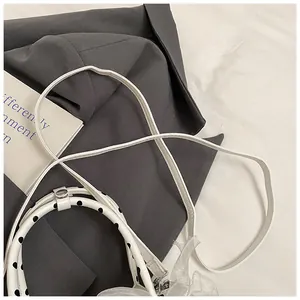 Detalle de bolso blanco con asa de lunares y un lazo elegante de organza translúcida