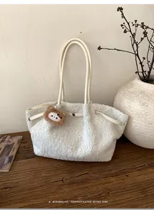 Detail of white faux fur tote bag with a small plush bear pendant on a wooden table