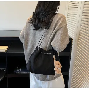 Detail of black quilted bucket bag featuring a chain strap and plush bear charm