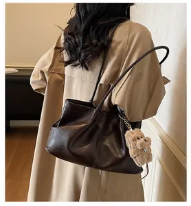 Détail d'un grand sac cabas en cuir marron avec breloque peluche sur trench-coat beige