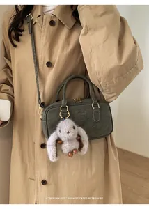 Detail of dark green retro mini Boston bag with plush bunny charm on khaki trench coat