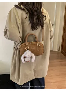 Side view of a brown vintage leather handbag with a cute white bunny charm on a beige trench coat
